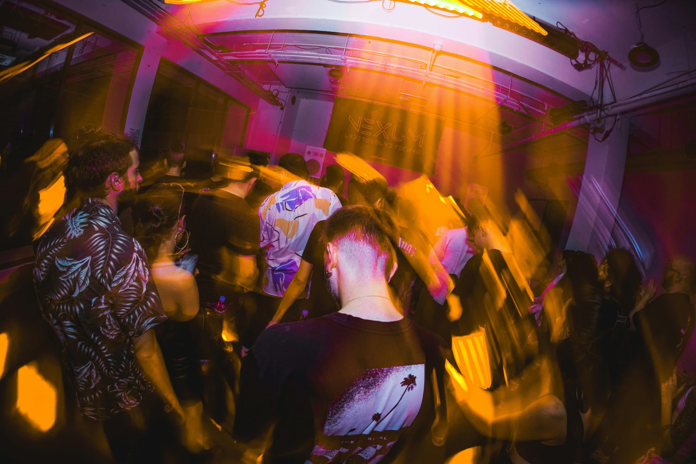 A crowded dance floor under pink and orange lights